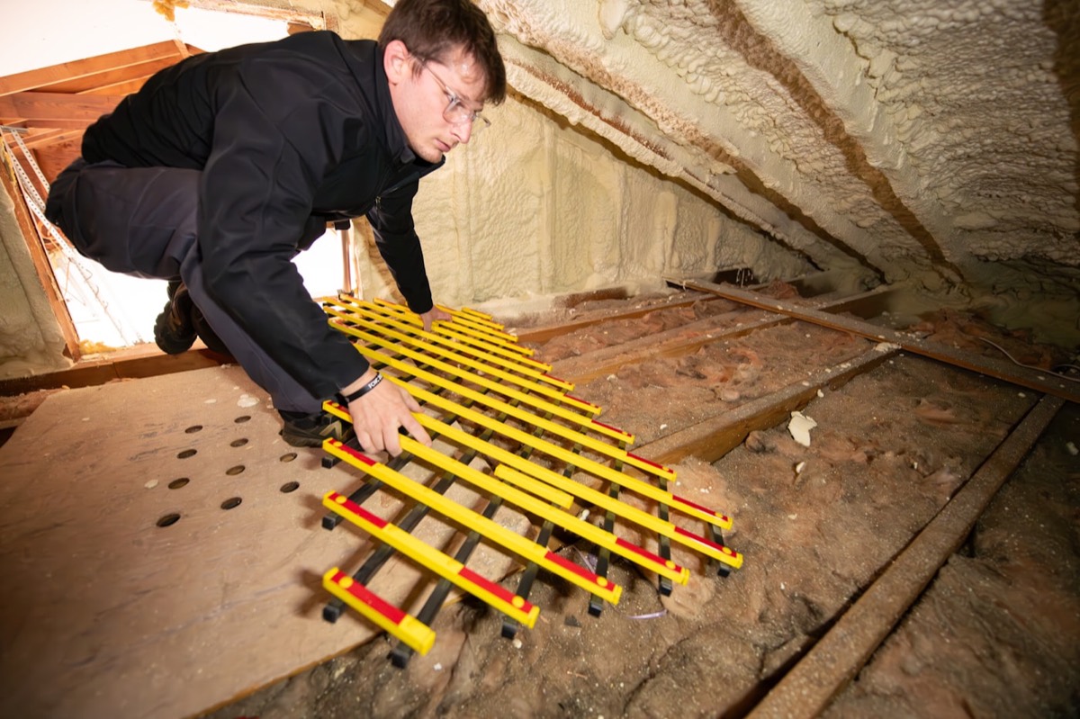 Technician working across an attic over insulation