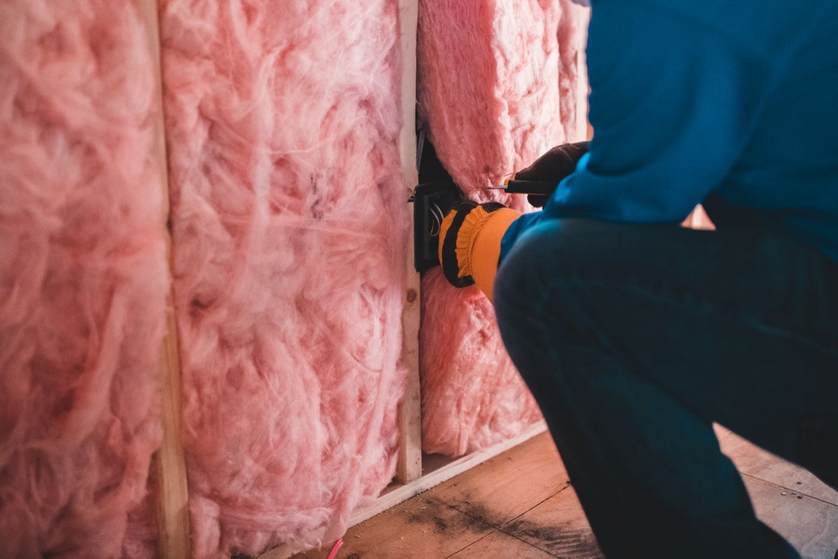Installer fitting fresh insulation between framing